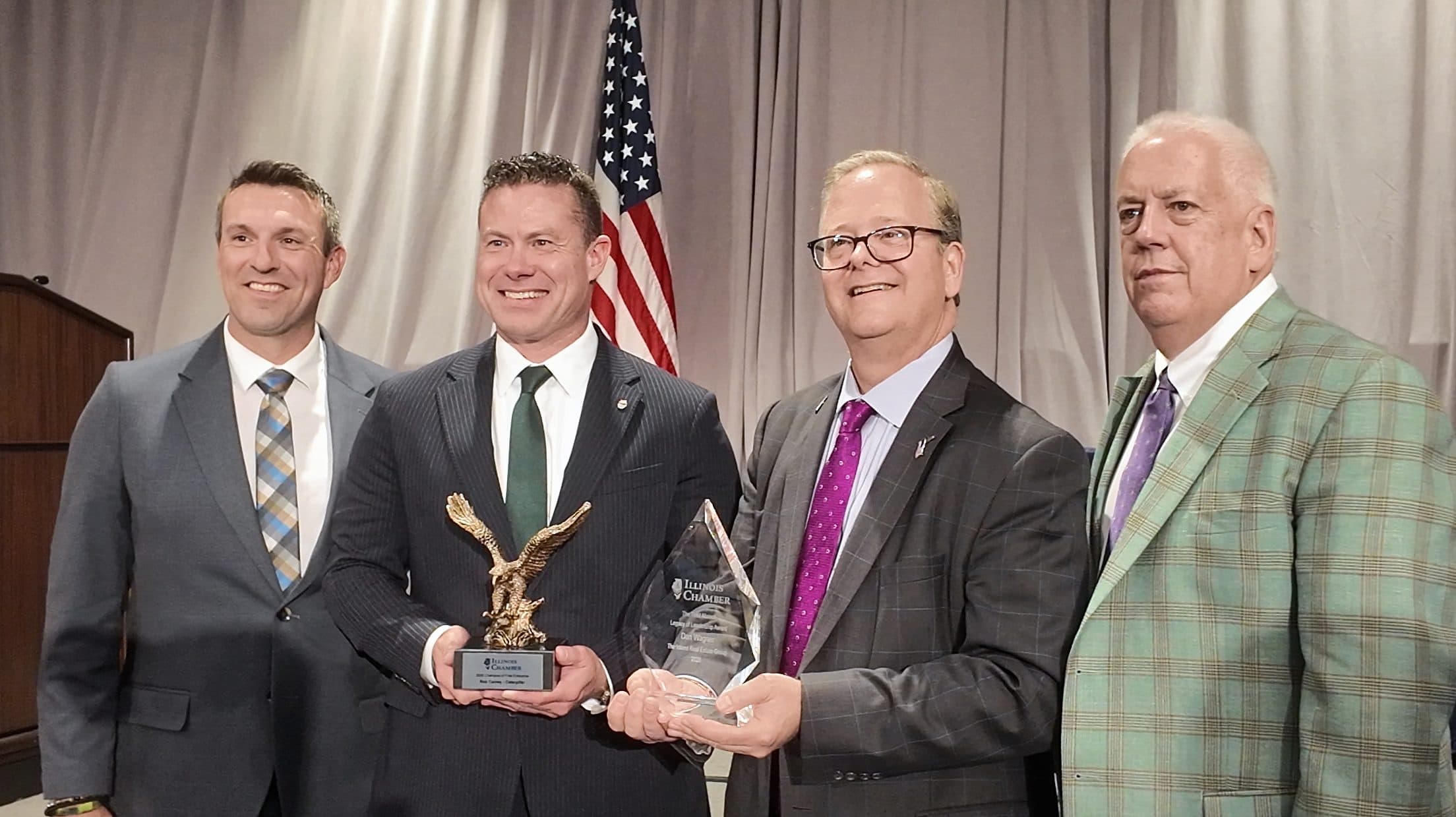Four men pose on stage with an eagle statuette and a crystal award.