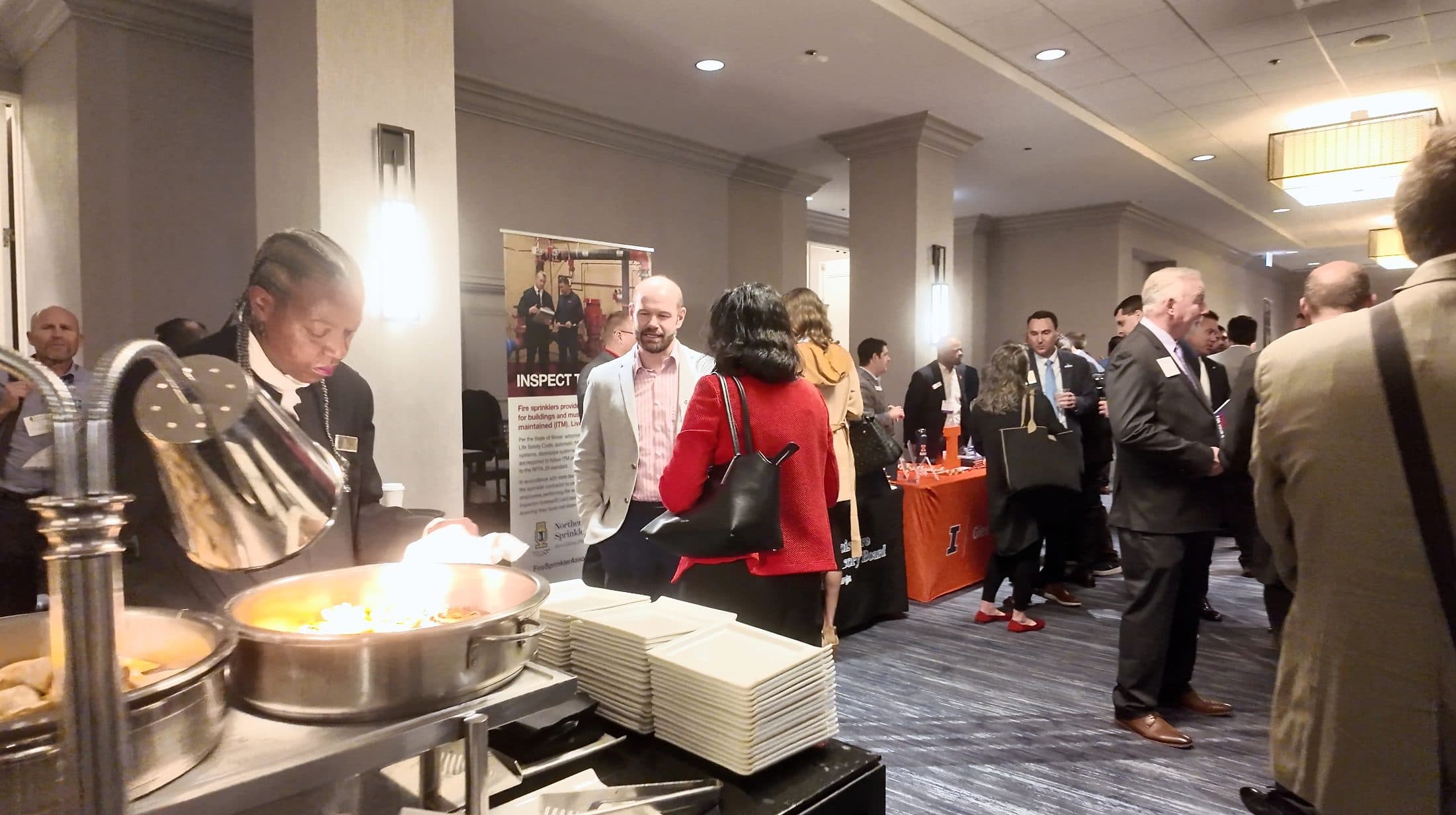 Attendees network in the expo hallway as a server tends the buffet.