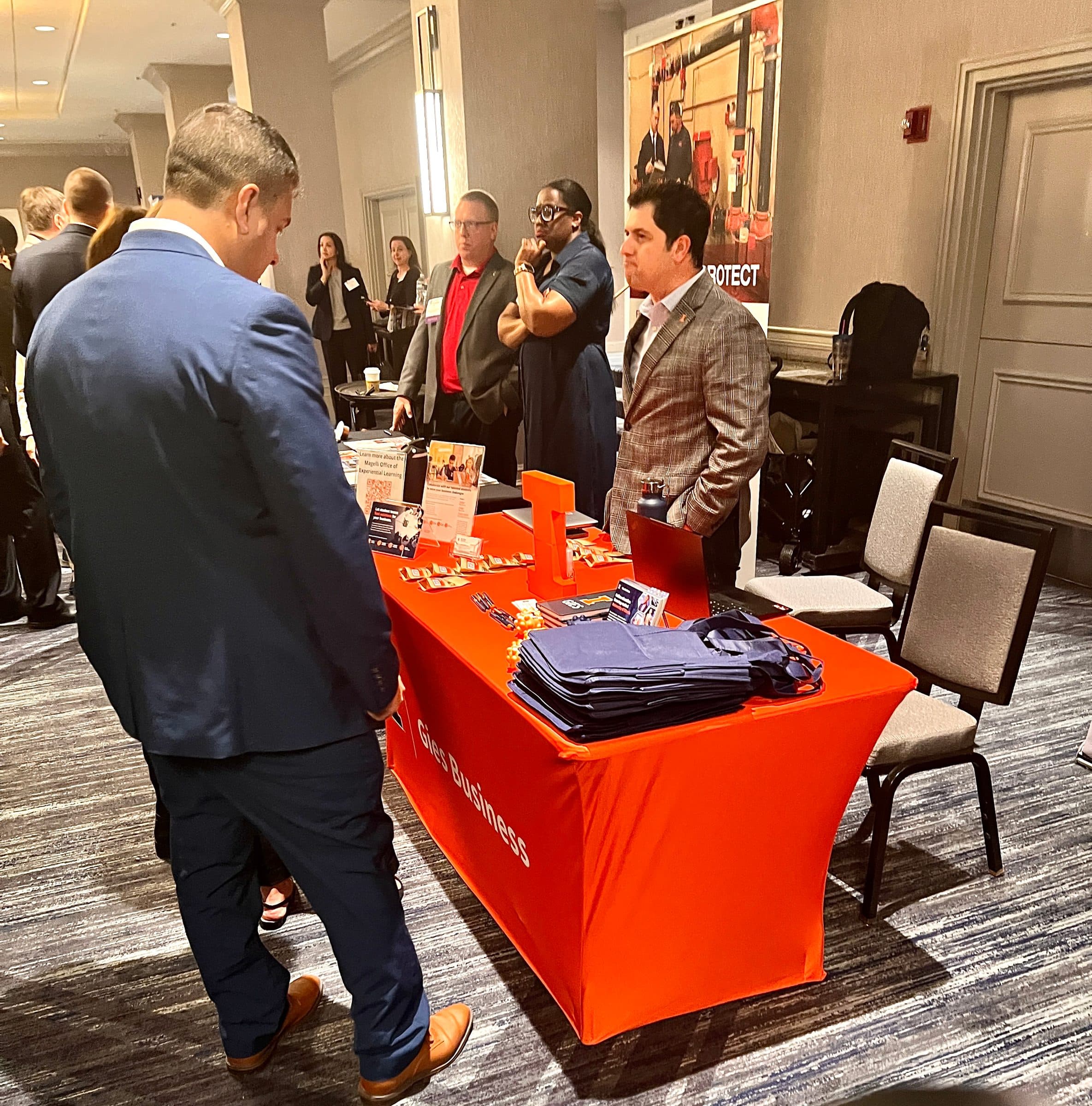 A visitor looks over an exhibitor table with an orange tablecloth.