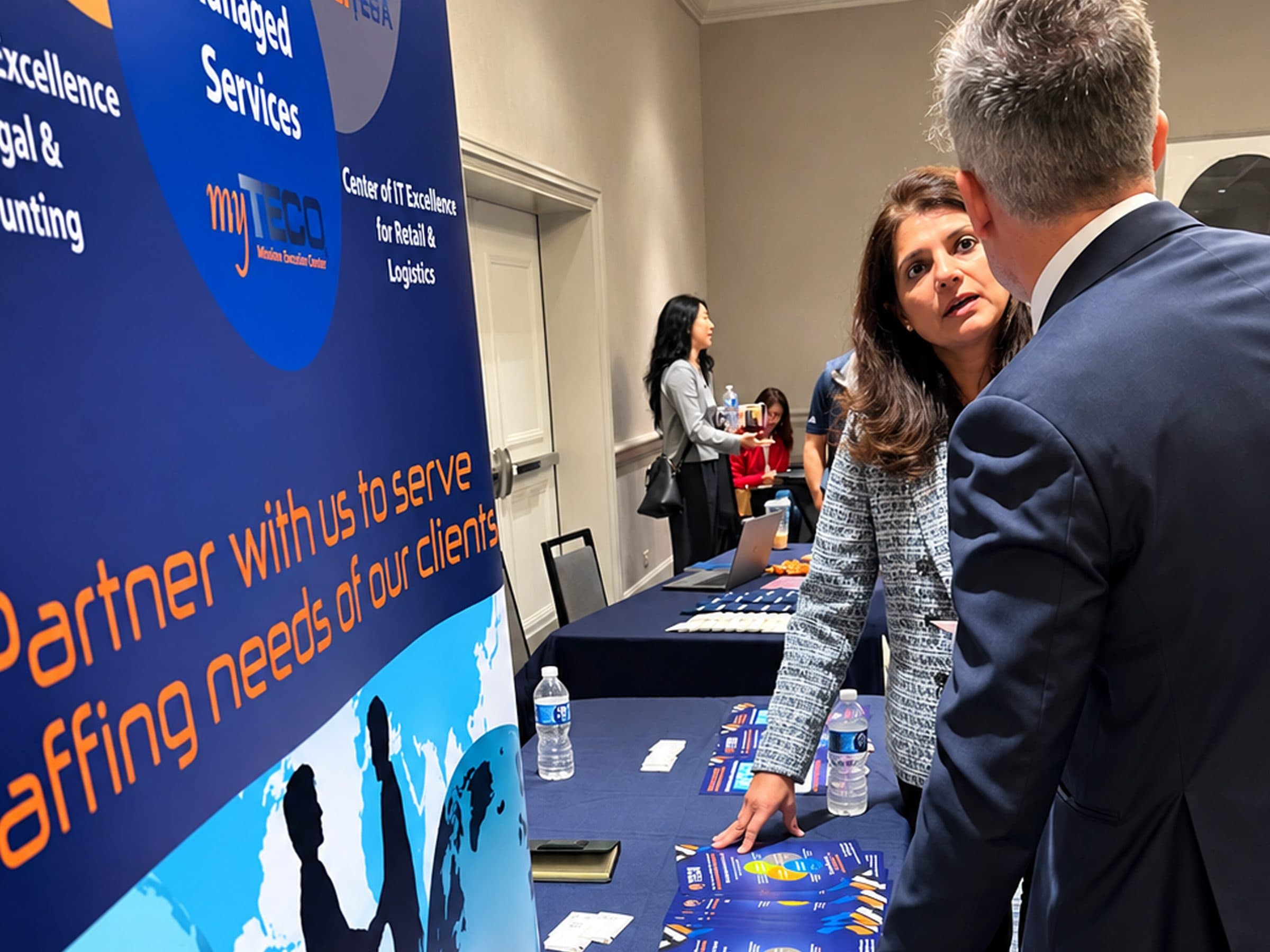 Two attendees talk at an IT and staffing services exhibit.