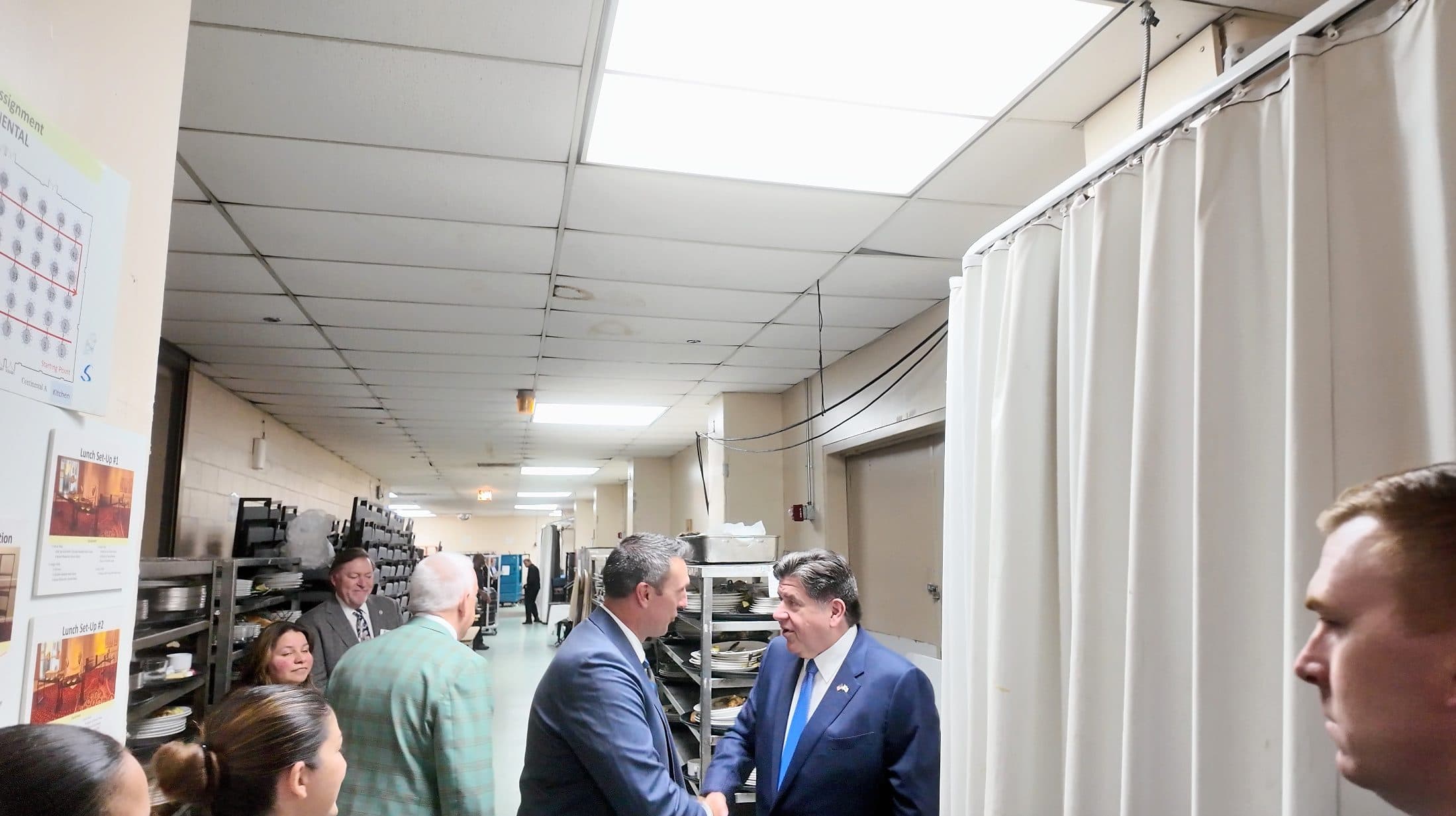 A guest is greeted with a handshake in a backstage service corridor.
