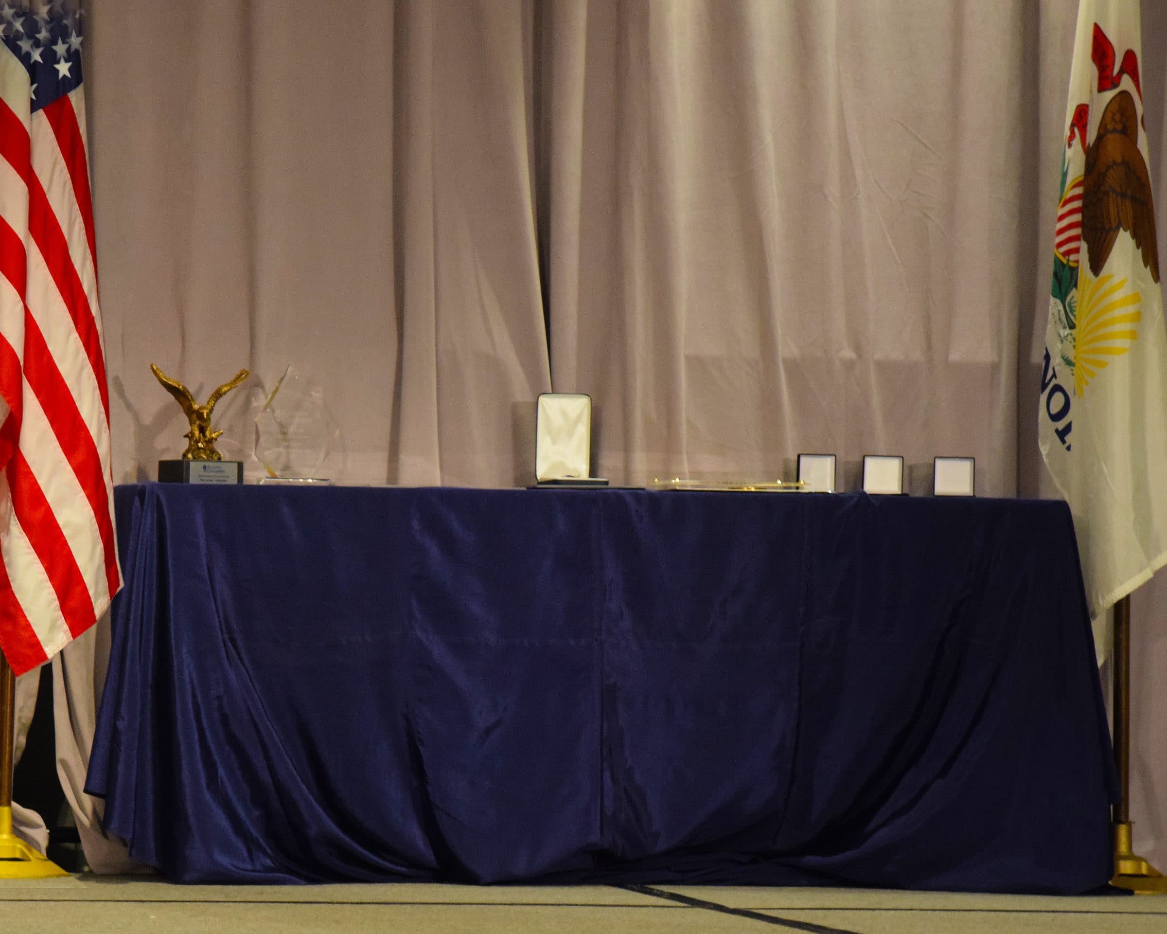 An awards table with an eagle statuette and plaques, set between the flags.
