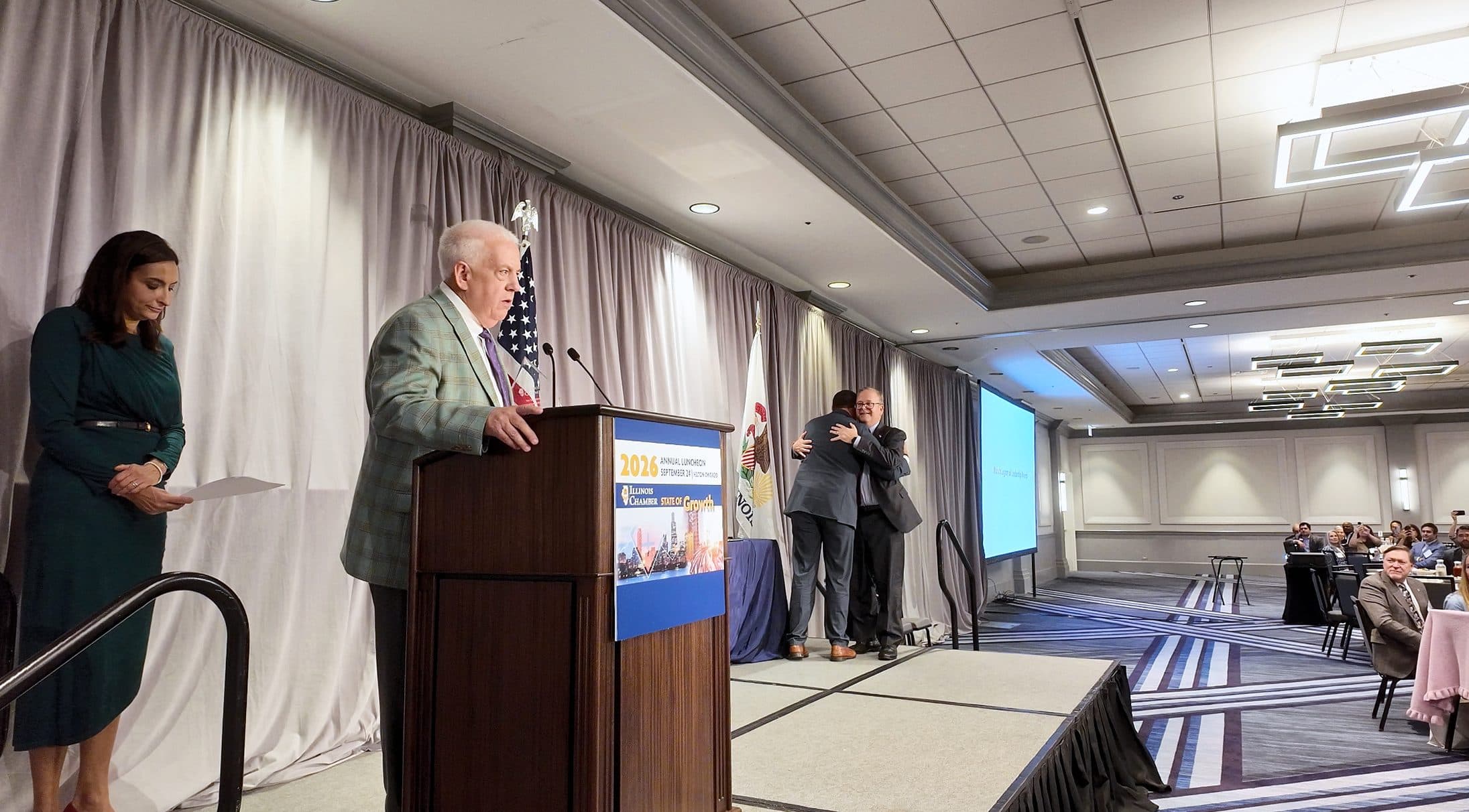 Two men embrace on stage beside the podium.