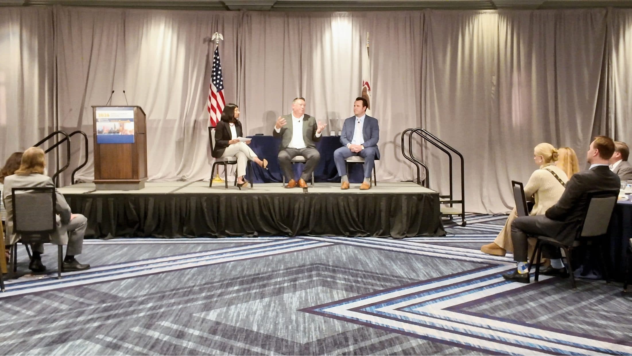 Three panelists in conversation on the luncheon stage.