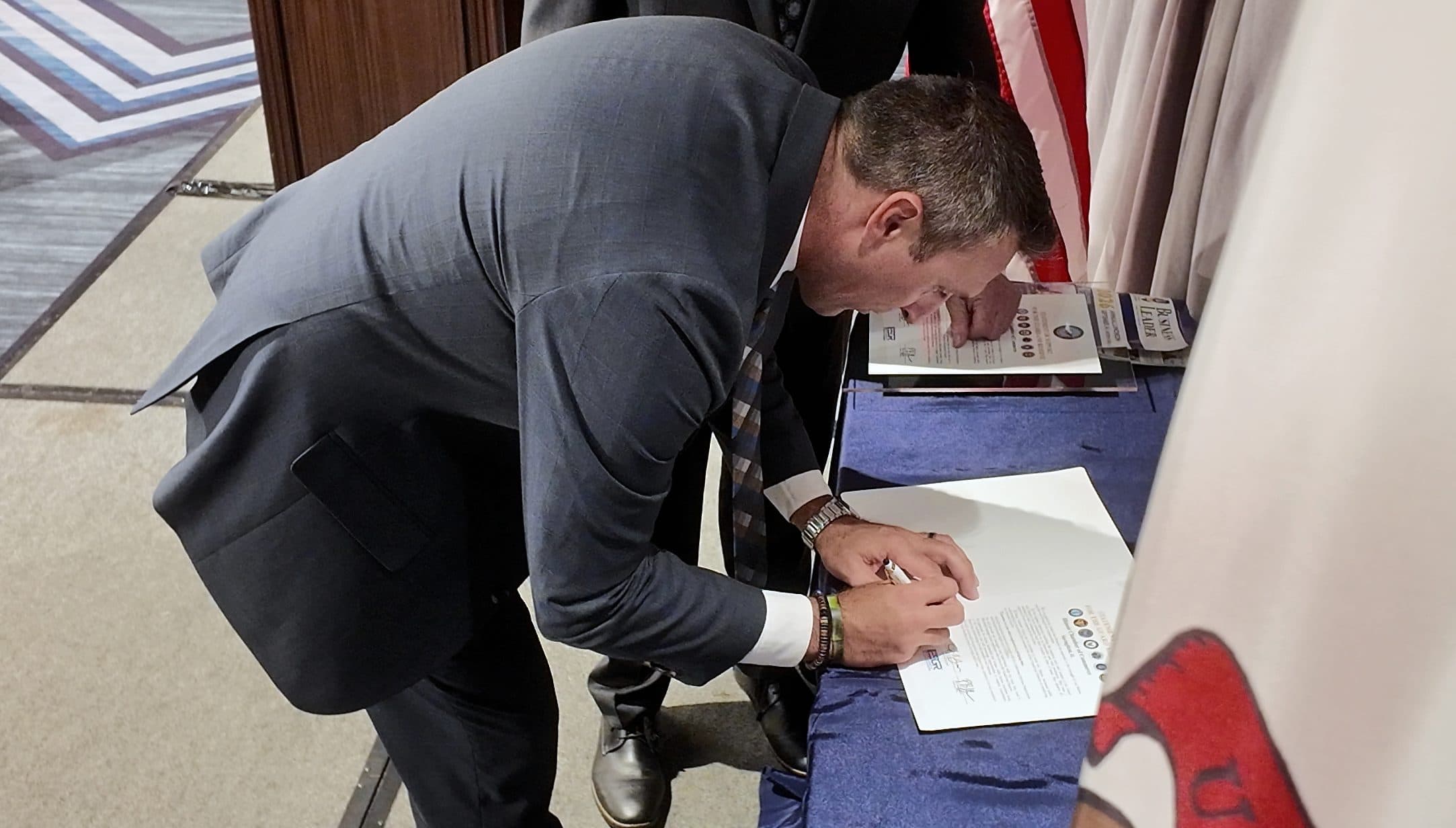 A man leans over a table to sign a certificate.