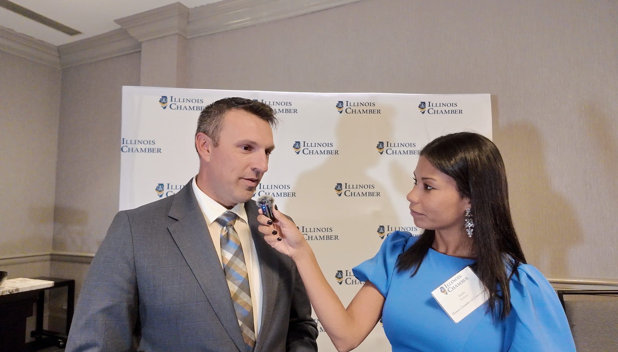 A reporter interviews a guest in front of the Illinois Chamber backdrop.