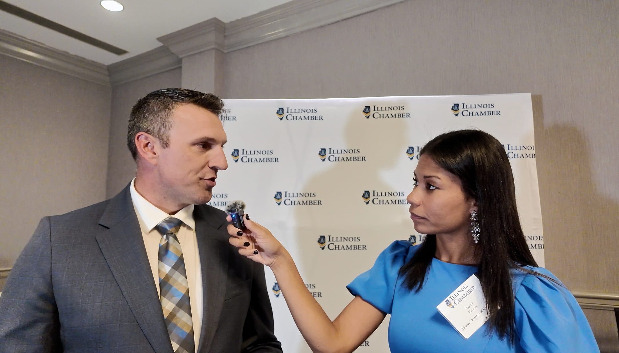 A guest answers a reporter's questions at the Illinois Chamber backdrop.